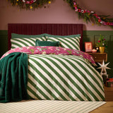 Reversible Feline Festive cotton duvet cover set with green and cream diagonal stripes, berry-red festive cat print trim, teal cushion and throw in a Christmas bedroom.
