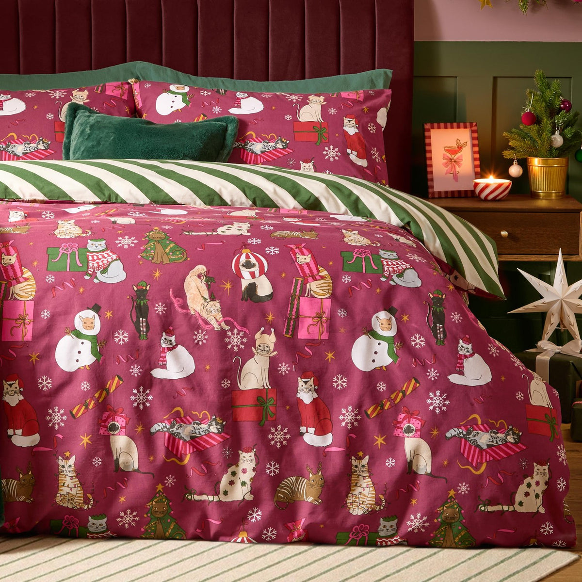 Purrgundy Feline Festive Cotton Striped Duvet Cover Set with berry-red cat print, green-and-cream striped reverse, styled on a bed with green cushions and Christmas décor.
