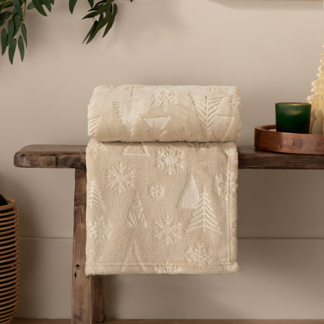 Natural beige polyester fleece throw, Festive Time Woodland design, folded on a wooden bench with embossed Christmas tree and snowflake motifs visible.