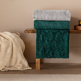 Festive Trees Woodland Polyester Throw in emerald green with embossed Christmas tree pattern, folded on a wooden bench beside a cream snowflake-textured throw.