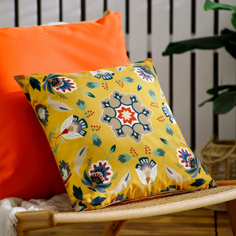 Folk Flora Floral Polyester Cushion in ochre-yellow with a folk-art medallion, floral and leaf print in teal, red and cream, shown propped on an orange sofa.