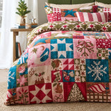 Fika Cotton Geometric Duvet Cover Set in Multi dressing a bed, featuring a reversible Christmas patchwork of stars, snowflakes and swans in pink, teal, red and olive, styled in a bedroom.