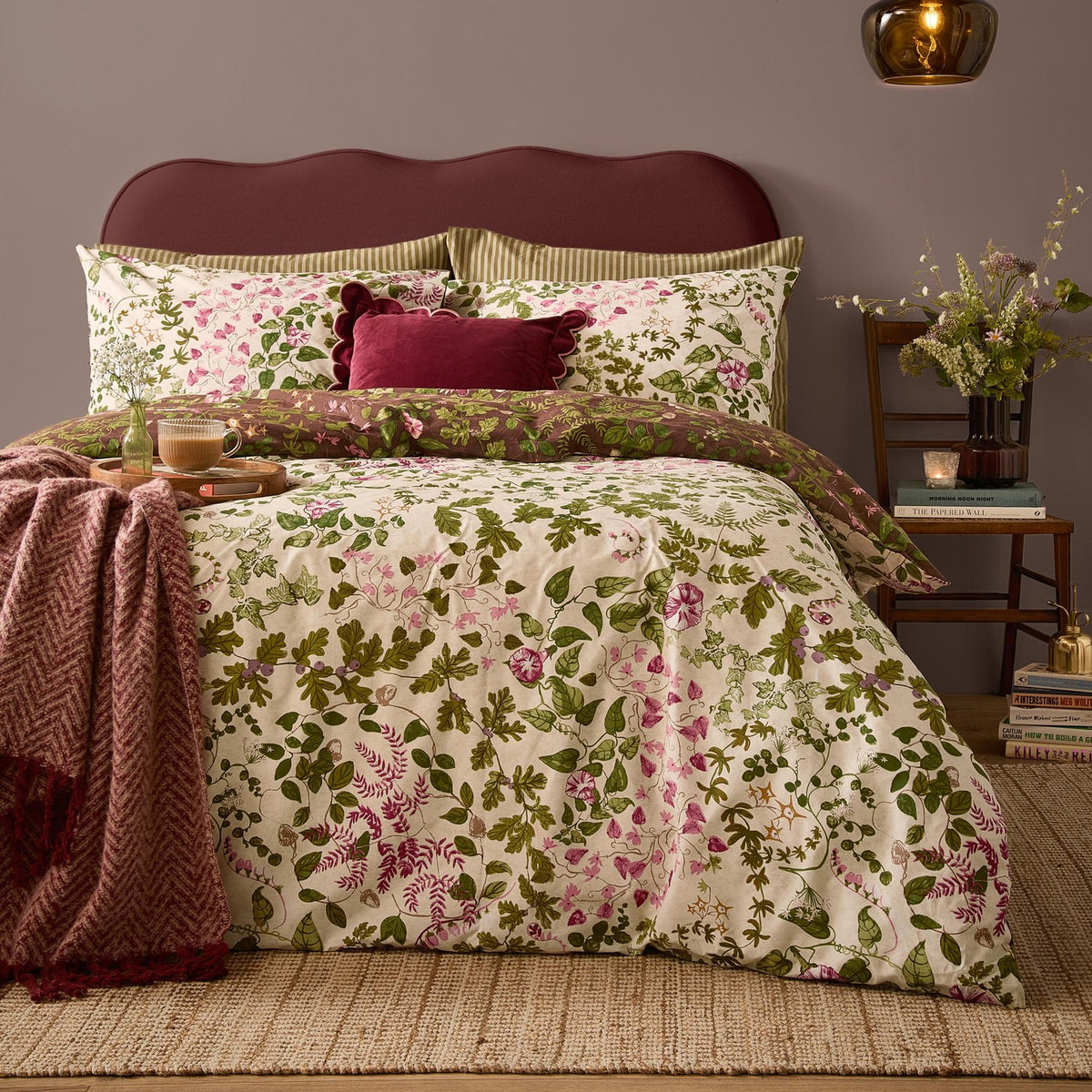 Flora Wilde Reversible Floral Duvet Cover Set in Chocolate, shown on a bed with cream pink and green wildflower print, burgundy velvet cushion, and dark red upholstered headboard.