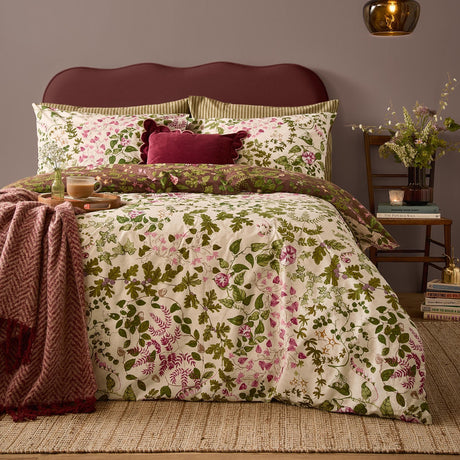 Flora Wilde Reversible Floral Duvet Cover Set in Chocolate, shown on a bed with cream pink and green wildflower print, burgundy velvet cushion, and dark red upholstered headboard.