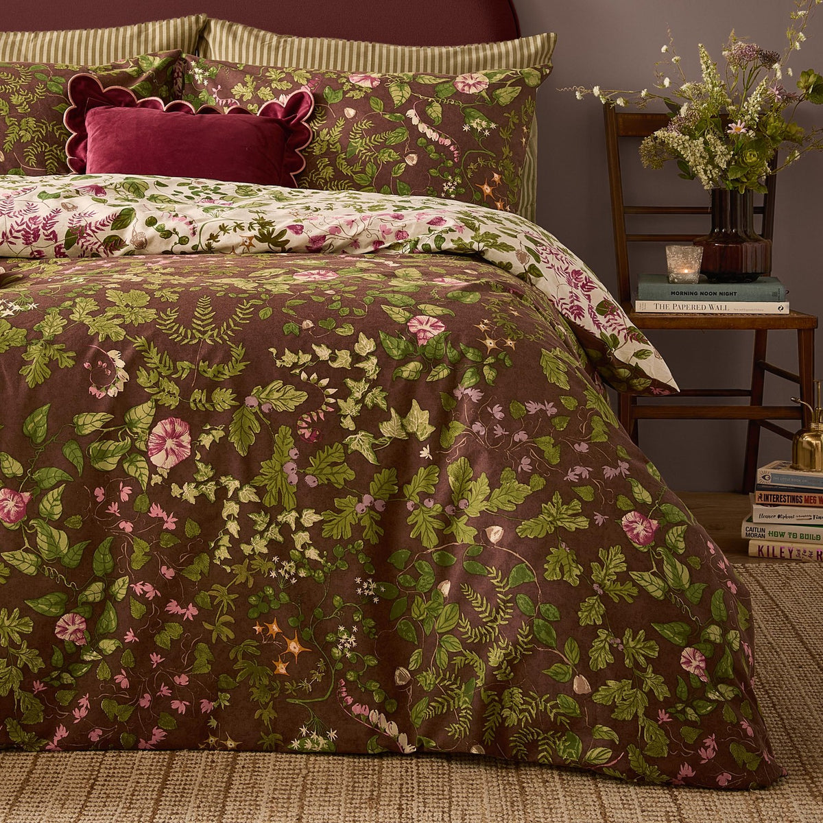 Flora Wilde Reversible Floral Duvet Cover Set in chocolate brown with pink and green wildflower print, styled on a bed with cream floral pillowcases in a bedroom setting.