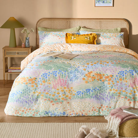 Florin Reversible Floral Duvet Cover Set in Multi on a bed with rattan headboard, showing a meadow floral print in blue, orange, lilac and pink with matching pillowcases.