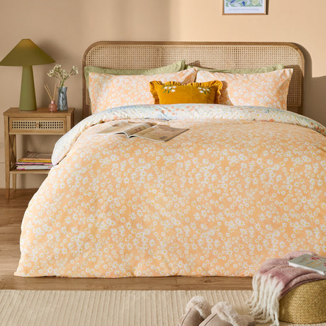 Florin Reversible Floral Duvet Cover Set in Multi, shown on a bed with matching pillowcases in apricot daisy print, styled in a bedroom with rattan headboard and side table.