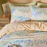 Florin Reversible Floral Duvet Cover Set in Multi, styled bed showing meadow floral pillowcases and duvet reversed to an apricot daisy print, on a rattan headboard bedroom setting.