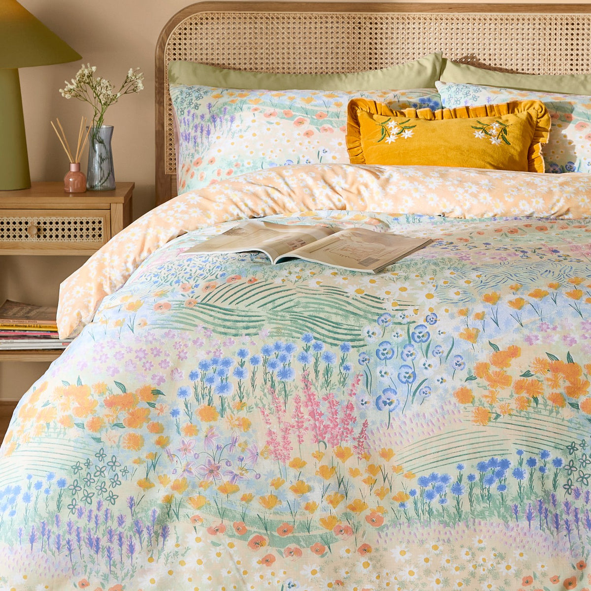 Florin Reversible Floral Duvet Cover Set in multicoloured meadow print with matching pillowcases, styled on a bed with a rattan headboard and mustard cushion.