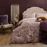 Floella Cotton Botanical Duvet Cover Set in dusky pink with cream and tan floral and bird print, styled on a bed with matching pillowcases in a deep plum bedroom.