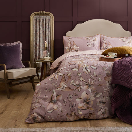 Floella Cotton Botanical Duvet Cover Set in dusky pink with cream and tan floral and bird print, styled on a bed with matching pillowcases in a deep plum bedroom.