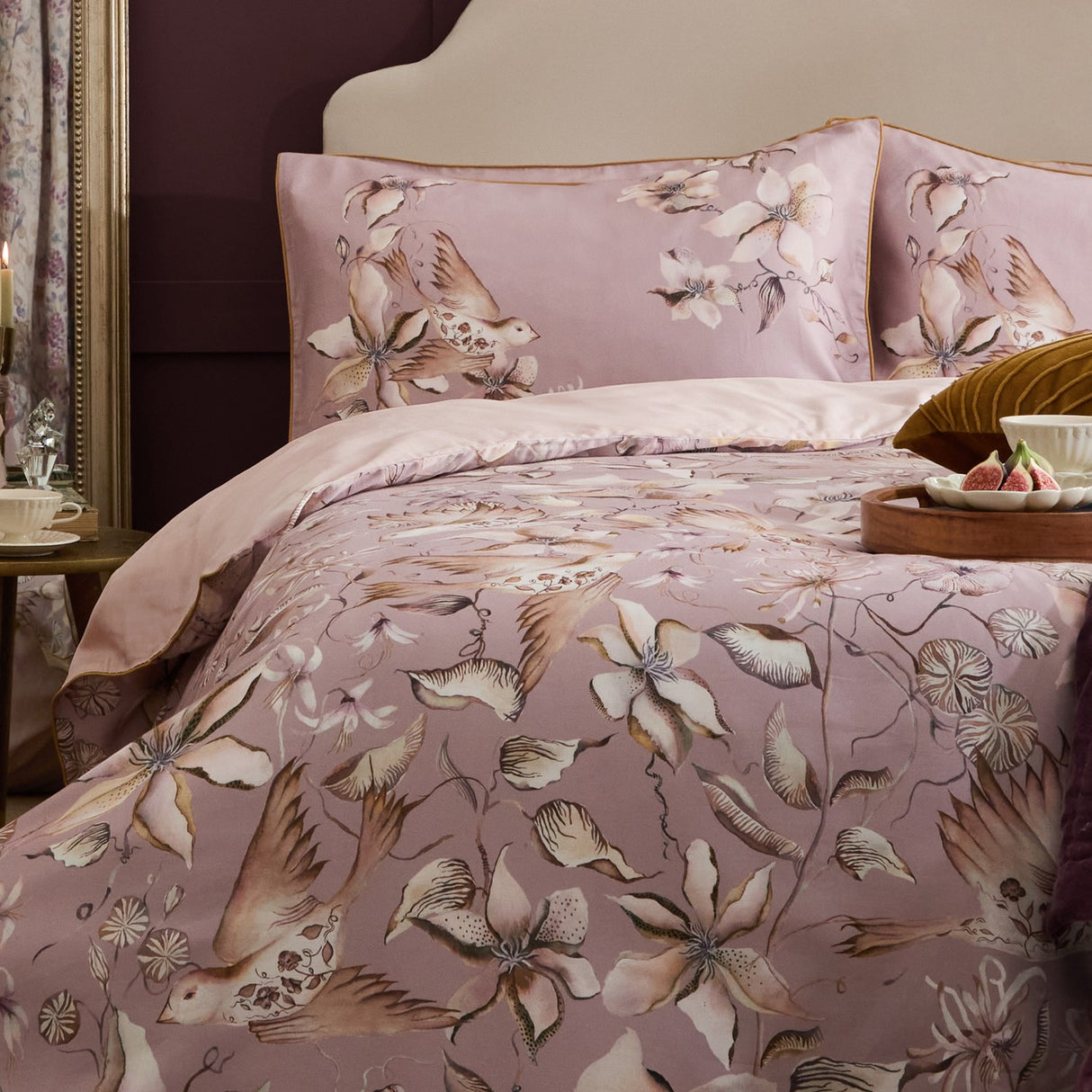 Floella Cotton Botanical Duvet Cover Set in dusky pink, styled on a bed with matching pillowcases showing a watercolour print of birds and trailing florals in cream and tan.