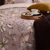 Floella Cotton Botanical Duvet Cover Set in purple, styled on a bed with a floral bird print in cream and mauve, mustard cushion and dark throw with a breakfast tray.