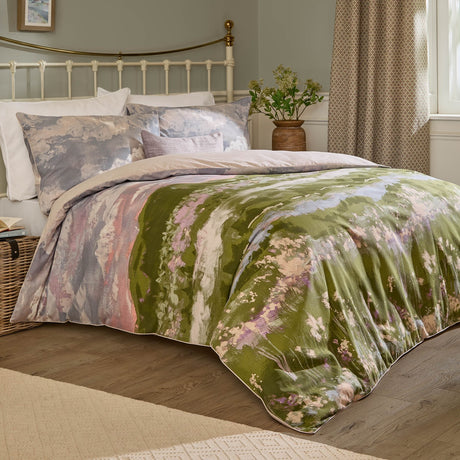 Foinaven Cotton Piped Duvet Cover Set in Heather on a bed, showing a painterly landscape print in mossy green, dusky pink and soft neutral tones with matching pillowcases in a bedroom setting.