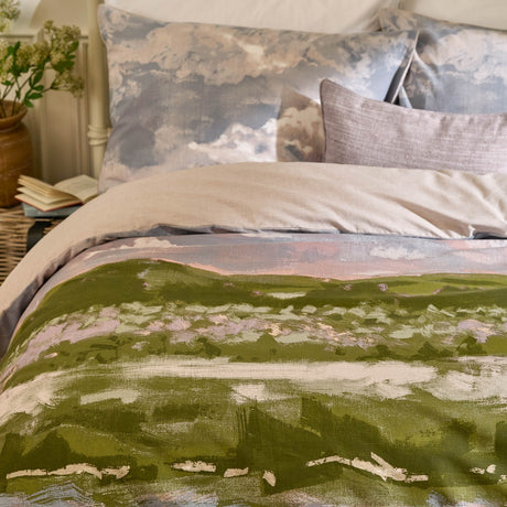 Foinaven Cotton Piped Duvet Cover Set in Heather, shown on a bed with a painterly green and pink landscape print, cotton-piped edge, and cloud-print pillowcases in a bedroom setting.