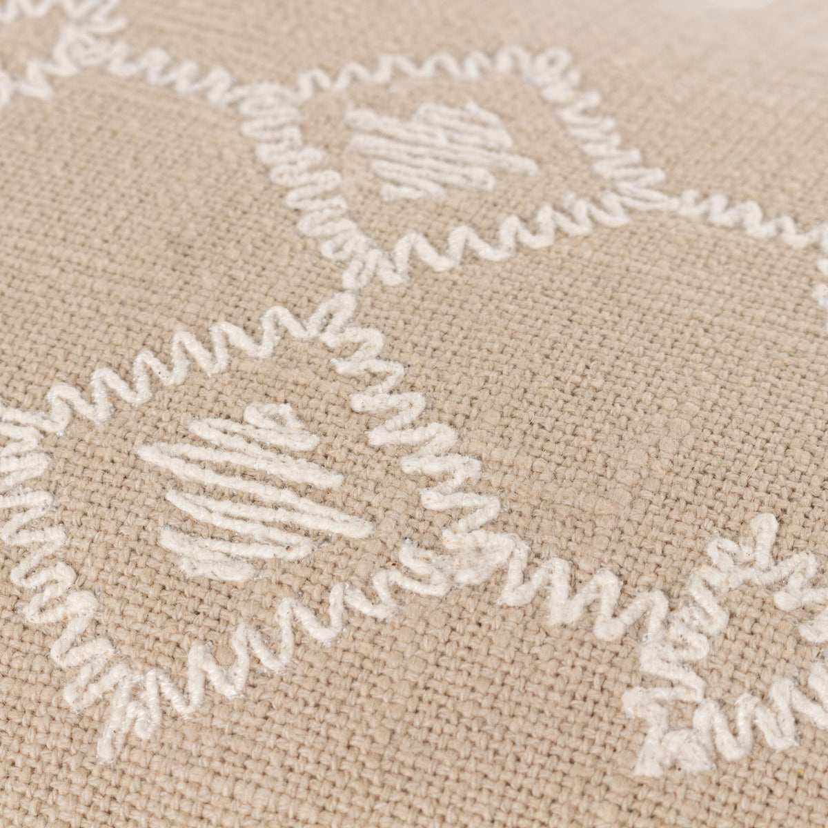 Close-up of the Folis Geometric Cotton Cushion in stone, showing raised cream embroidered diamond and cross motifs on a slubby beige cotton base.