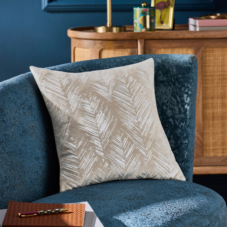 Folius Velvet Cotton Cushion in silver, square with a foil-printed herringbone leaf pattern on a warm neutral velvet face, styled on a blue upholstered chair.