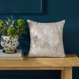 Folius Velvet Cotton Cushion in silver, a 43 x 43cm square with a foil-printed herringbone leaf pattern, shown on a wooden bench against a dark blue wall.