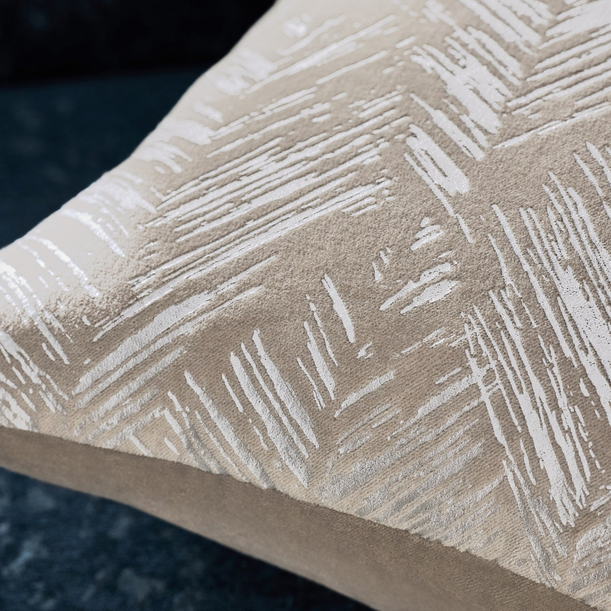 Close-up of the Folius Velvet Cotton Cushion in silver, showing a foil-printed herringbone leaf pattern on cotton velvet in warm neutral tones, with a plain edge seam visible.