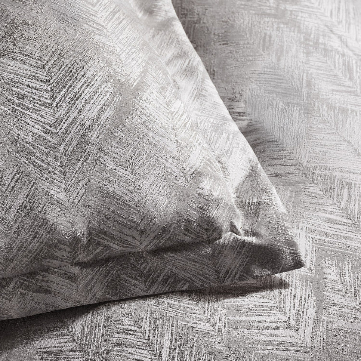 Folius Cotton Leaf Duvet Cover Set in silver, close-up of pillow and bedding showing a woven leaf jacquard pattern with a textured, shimmering finish.