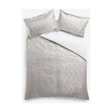 Folius Cotton Leaf Duvet Cover Set in silver on a bed, showing a jacquard woven leaf pattern with matching pillowcases against a plain white background.