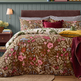 Chocolate Forest Bloom reversible duvet set with floral, wildflower and mushroom print, cream reverse, striped pillowcases and burgundy velvet cushions on a bed.