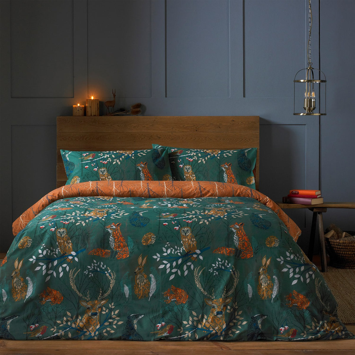 Emerald Forest Fauna duvet cover set with matching pillowcases, printed with foxes, hares, stags and owls among leaves, rust reverse visible at the fold, shown on a bed in a dark bedroom.
