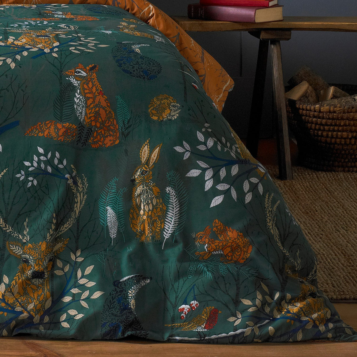 Forest Fauna Woodland Animal Duvet Cover Set in Emerald, showing foxes, hares, stags and hedgehogs printed on deep green cotton with a rust reverse edge visible, styled on a bed indoors.