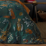 Forest Fauna Woodland Animal Duvet Cover Set in Emerald, showing foxes, hares, stags and hedgehogs printed on deep green cotton with a rust reverse edge visible, styled on a bed indoors.
