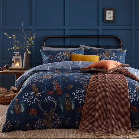 Forest Fauna Woodland Animal Duvet Cover Set in navy on a bed, printed with a stag, fox, owl and hare among leaves, styled with rust and mustard cushions and a checked throw.