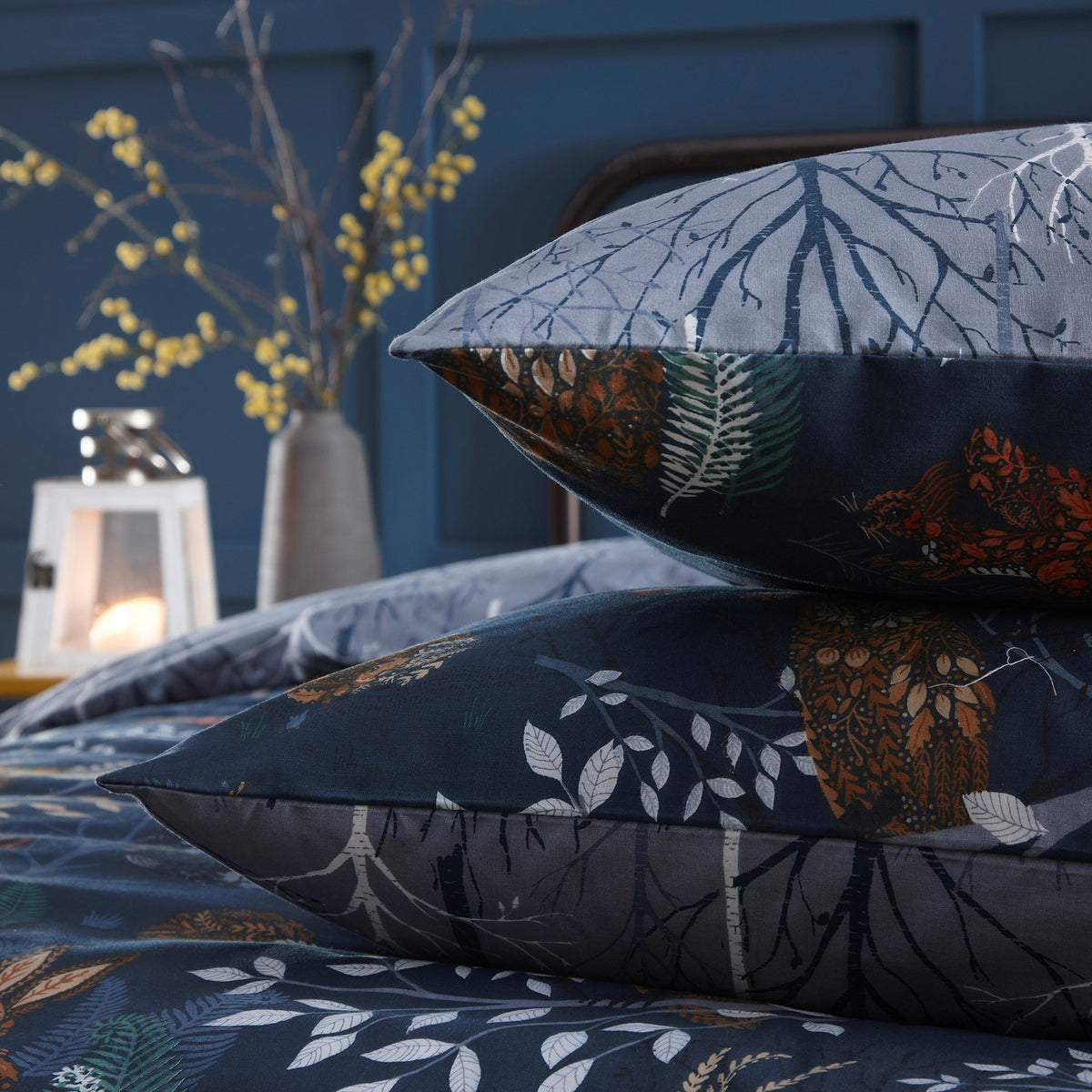 Forest Fauna Woodland Animal Duvet Cover Set in navy, showing stacked pillowcases with woodland animal and leaf prints on one side and bare tree branch design on the reverse, styled on a bed.