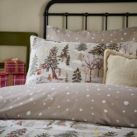Forest Festivities cotton duvet cover set on a bed, reverse spotted natural side shown with pillowcase featuring a printed woodland Christmas scene of trees, animals and fairy lights.