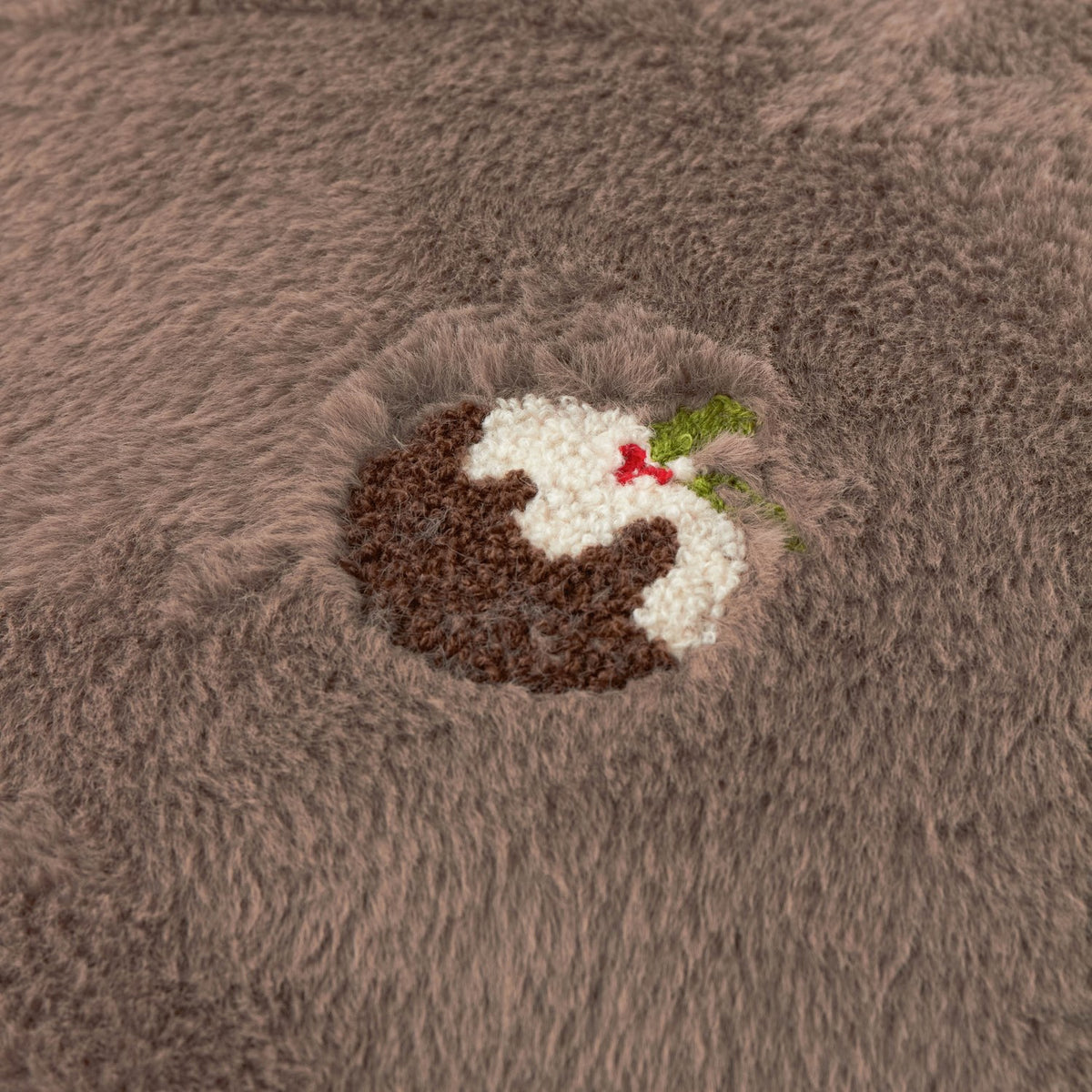 Close-up of the Festive Puddings Embroidered Faux Fur Cushion in mocha, showing a raised embroidered Christmas pudding with holly on plush brown faux fur.