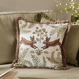 Fable Rabbits Woodland Cotton Cushion in willow green, square with fringe trim, showing two leaping rabbits and fern motifs, styled on a sofa.