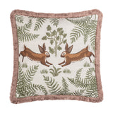 Fable Rabbits Woodland cotton cushion in willow green, square with pink fringe trim, featuring two mirrored leaping rabbits amid ferns and foliage on a cream ground, shown on a plain white background.