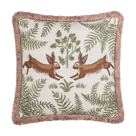 Fable Rabbits Woodland cotton cushion in willow green, square with pink fringe trim, featuring two mirrored leaping rabbits amid ferns and foliage on a cream ground, shown on a plain white background.