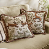 Fable Rabbits Woodland cotton cushion in willow green with fringe trim, showing leaping rabbits and fern motifs, styled on a sofa beside a matching deer-print cushion.