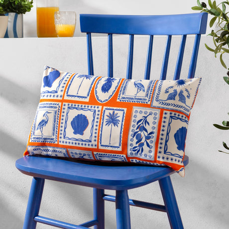 Frieze Abstract Polyester bolster cushion in coral and blue, printed with Greek island motifs like shells, palms and herons, shown on a blue chair.