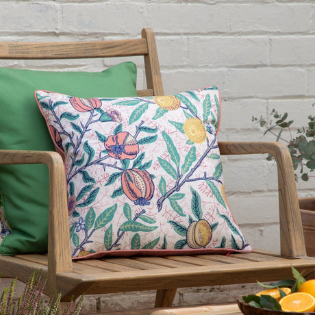 Fruits Piped Polyester Cushion in Coral/Lemon, square with pomegranate and citrus print, green leaves and coral piped trim, shown on a wooden garden bench.