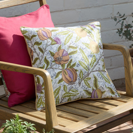 Fruits Piped Polyester Cushion in Lemon/Lime, square with cream ground and green, apricot and lilac pomegranate print, piped edges, shown on a wooden bench beside a pink cushion.