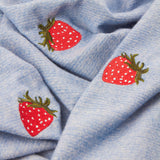 Fruits Knitted Polyester Throw in Berry Sweet Blue, close-up of chambray-blue fabric with embroidered red strawberry motifs and green calyx detailing.