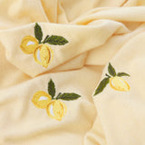 Close-up of the Fruits Knitted Polyester Throw in Zesty Lemon, showing pale yellow knitted fabric with embroidered lemon motifs in yellow and green thread.