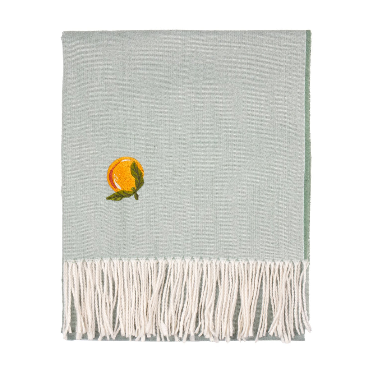 Sage green knitted polyester throw with an embroidered orange citrus motif and leafy sprig, finished with long cream tassels along one edge, shown folded on a plain white background.