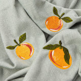 Close-up of the Fruits Knitted Polyester Throw in sage green, showing embroidered orange citrus motifs with green leafy sprigs on the knitted fabric.