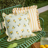 Fruits Gingham Polyester Cushion in Sage, a square scatter cushion with lemon print on pale green check, scalloped edge and yellow piped trim, shown on a green garden bench.