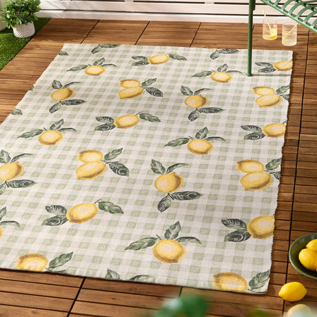Fruits Gingham Polyester Rug in Sage, a rectangular rug with a lemon and green leaf print on a sage and cream check, shown outdoors on a wooden deck.