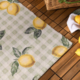 Fruits Gingham Polyester Rug in Sage, showing a sage and cream check pattern with painted lemon and green leaf motifs, displayed on a wooden deck.