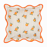 Square polyester cushion with scattered orange fruit print on cream and yellow striped fabric, edged with a wavy orange piped trim, shown on a white background.