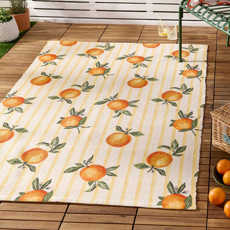 Fruits Gingham Polyester Rug in yellow, featuring orange fruit and leaf print on cream and yellow stripes, shown on an outdoor wooden deck.