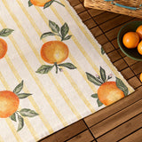 Fruits Gingham Polyester Rug in yellow, cream ground with hand-painted orange fruit and leaf print on yellow stripes, shown on a wooden deck beside a fruit bowl.